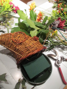 Gather the materials and remember to start at the base with greens to cover the oasis, then add accent pieces & flowers.